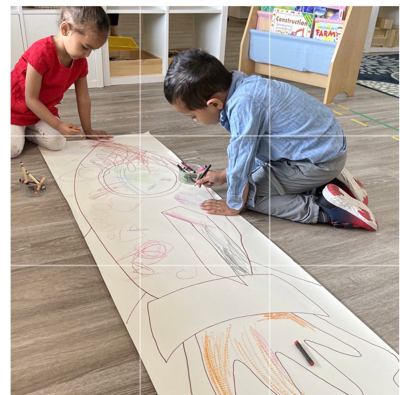 Two children drawing a large rocket together on a long sheet of paper