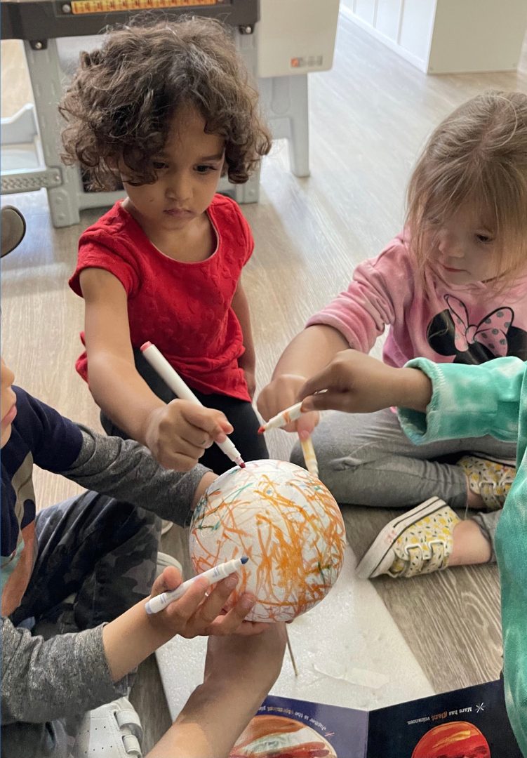 Preschoolers colouring a paper-mache globe with markers