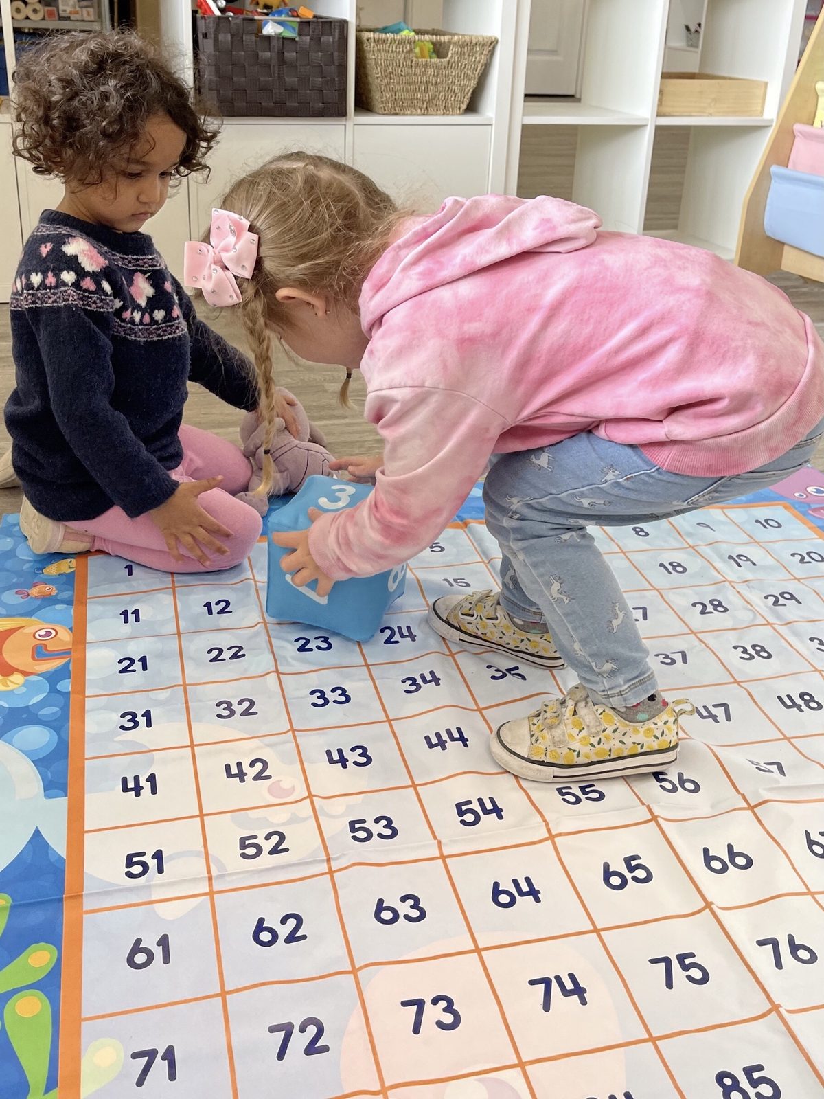 Two girls playing a number-grid dice game on the classroom floor