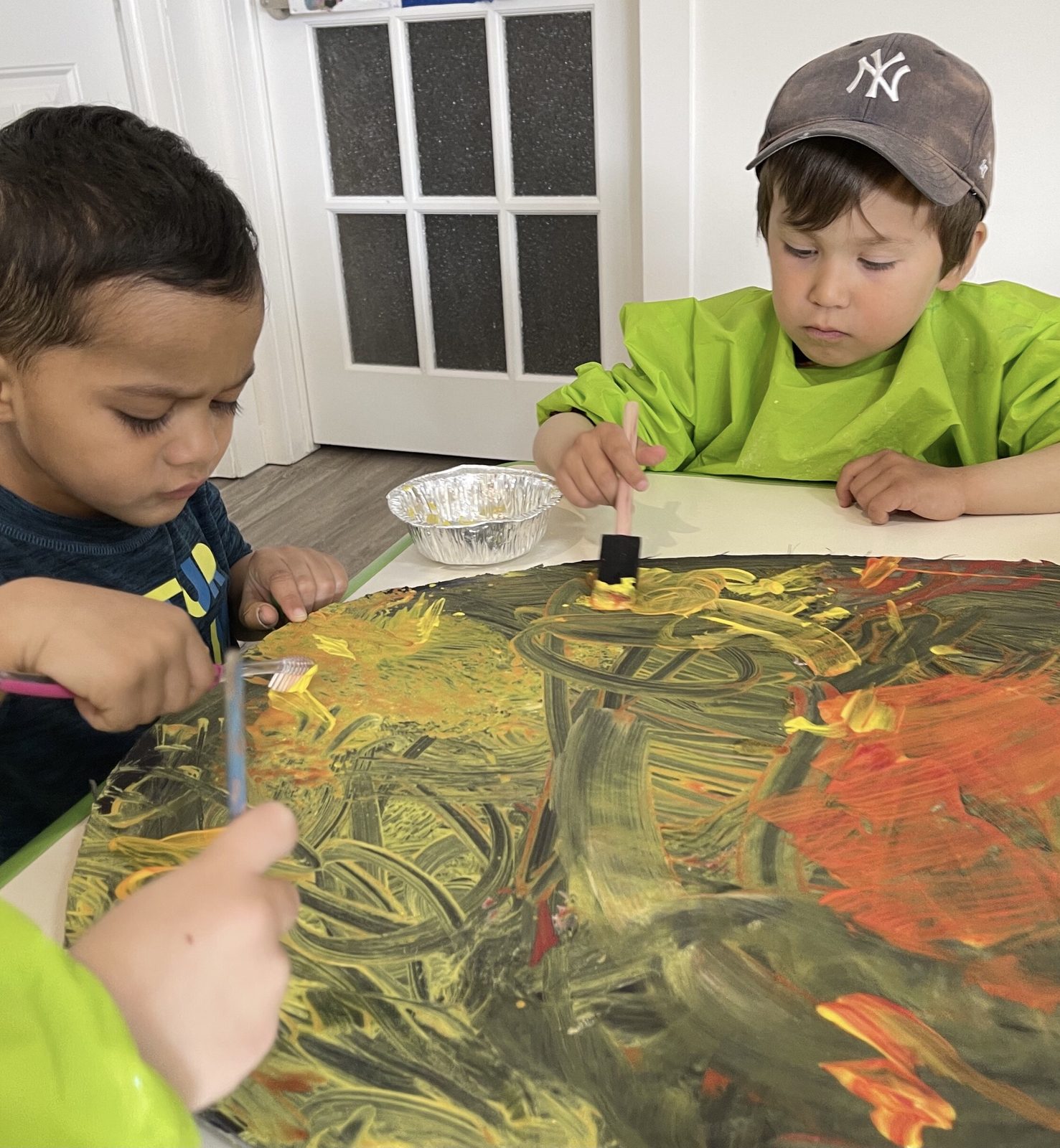 Two children in green smocks painting a large canvas together