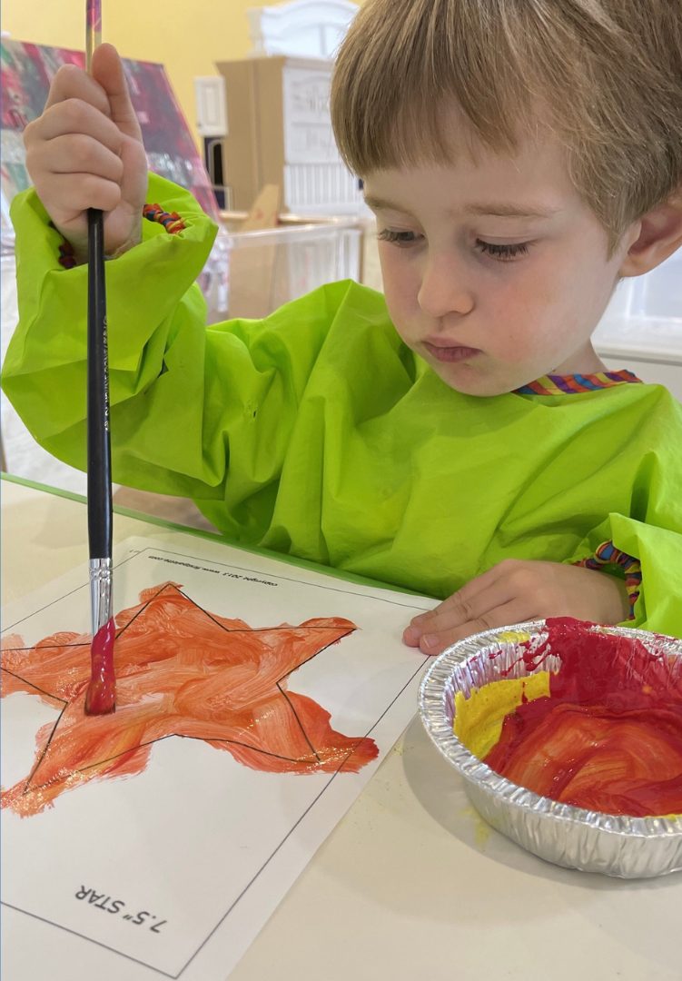 A boy painting a bright orange paper star