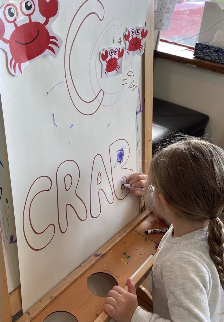 A girl writing the word crab on a classroom whiteboard